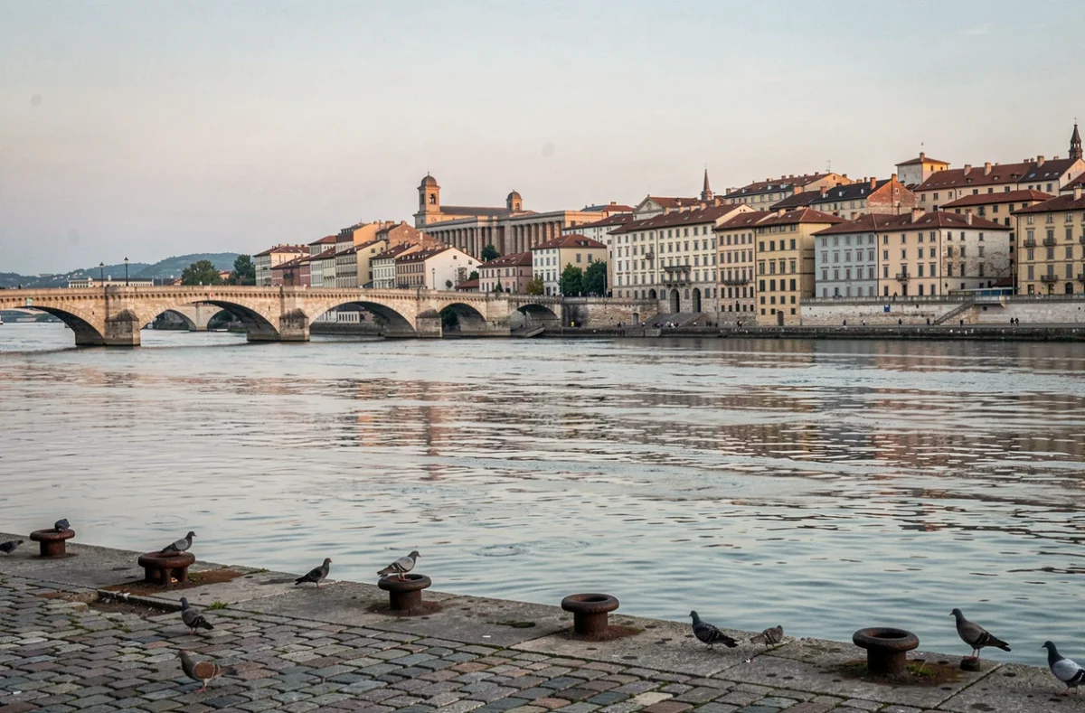 Vue sur le Rhône à Lyon avec un pont historique en pierre et les toits de la vieille ville se reflétant dans l'eau calme du fleuve